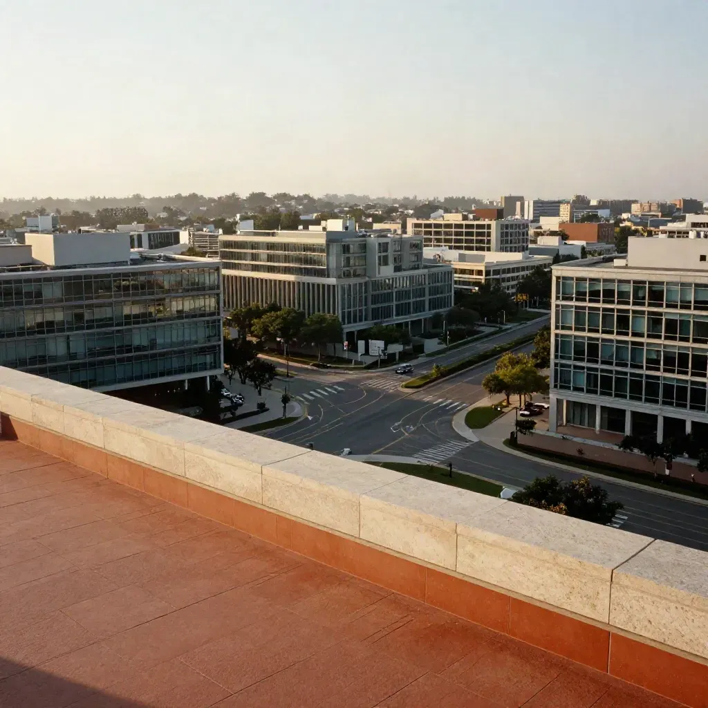 Hazy urban horizon of roads and low-rise glass above a calm stone foreground at sunrise