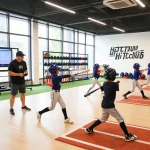 Young athletes practicing baseball techniques at hitclub facility with coaches guiding them.